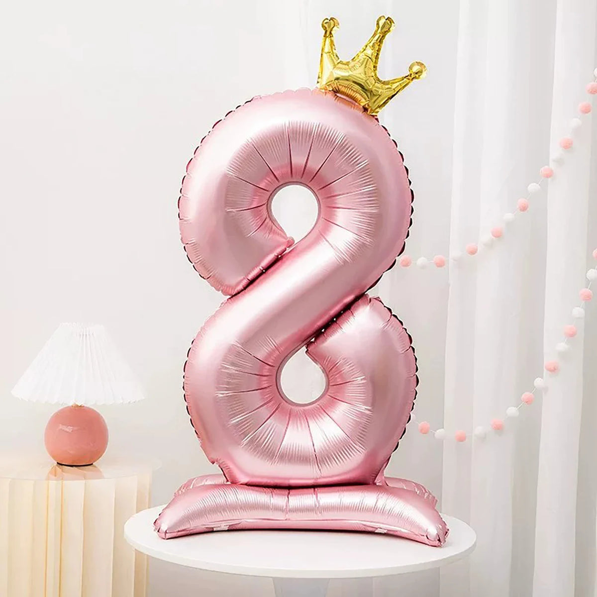 A pink foil balloon shaped like the number 8 with a gold crown on top