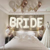 Elegant white and gold balloons spelling the word BRIDE above a bridal bed setup
