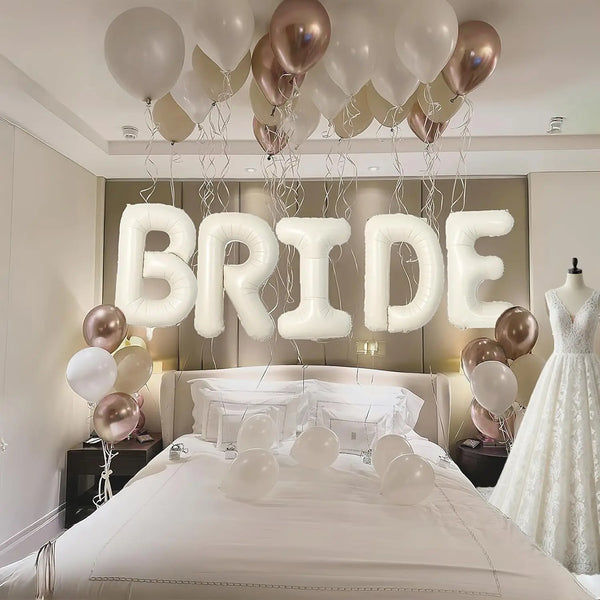 Elegant white and gold balloons spelling the word BRIDE above a bridal bed setup