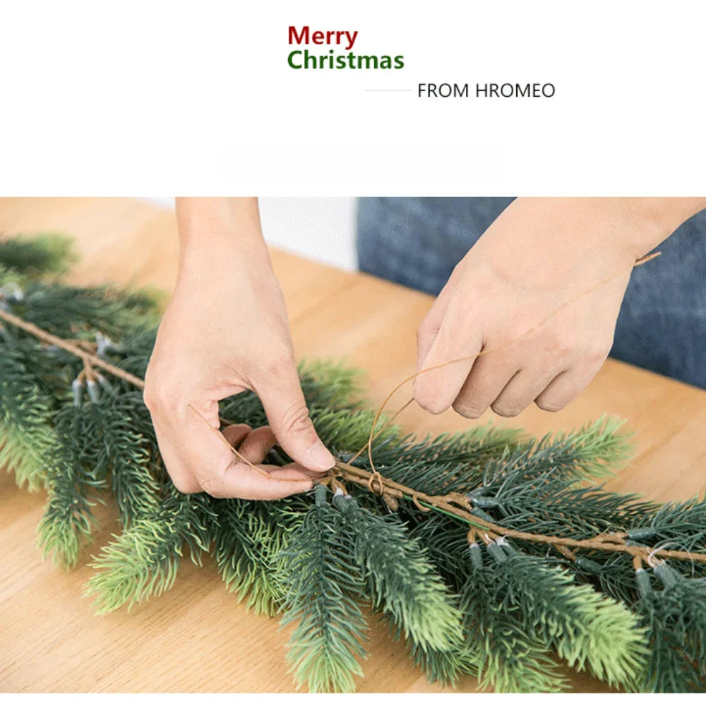Hands are arranging a green artificial pine garland on a wooden surface for holiday styling.