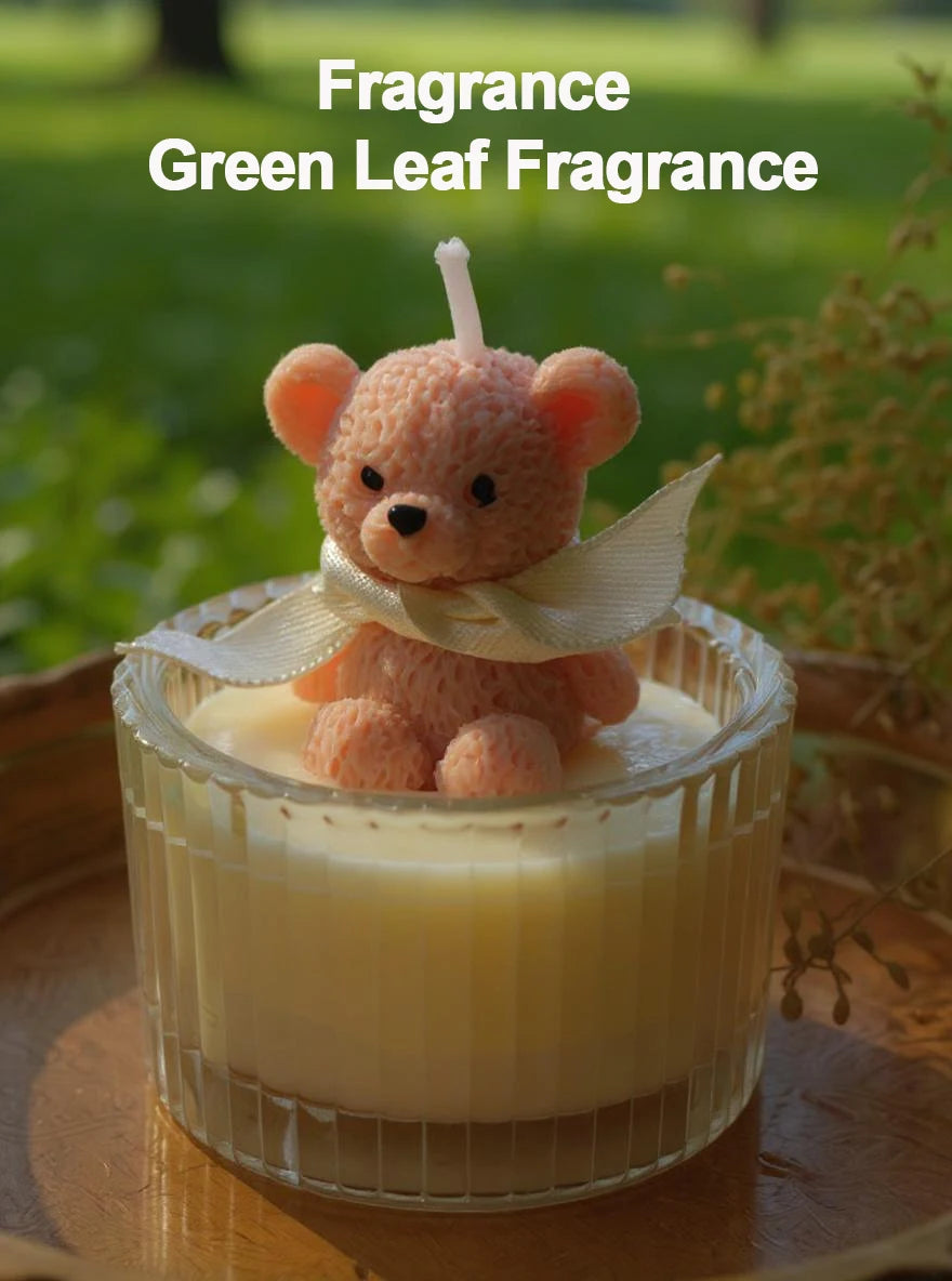 A pink teddy bear candle in a glass jar with a white ribbon set against a green outdoor background.
