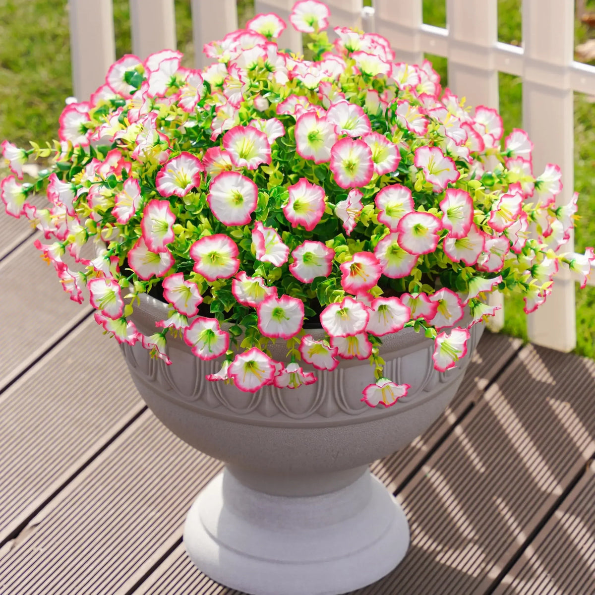 A potted arrangement of pink and white morning glory flowers and eucalyptus stems in a gray urn on a wooden deck.