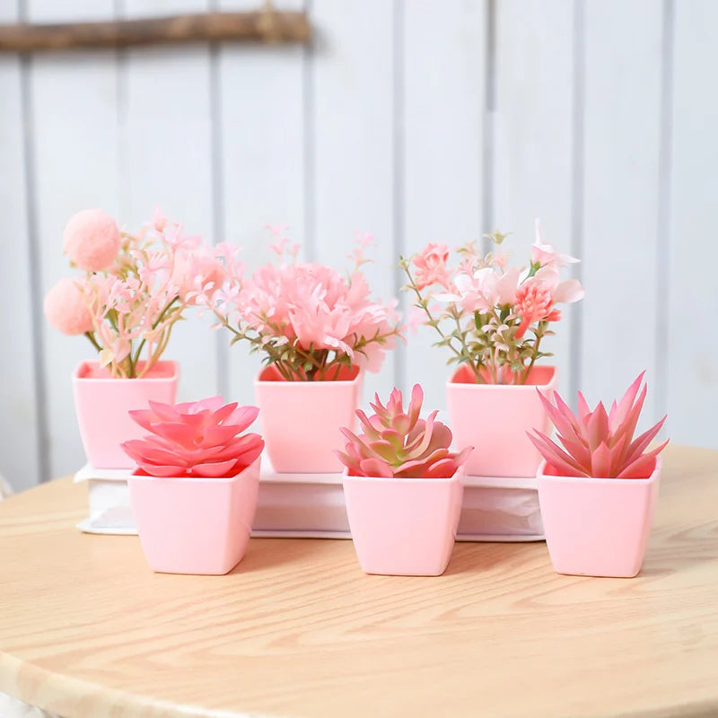 A set of six pink artificial succulent plants in small pots arranged on a wooden surface.