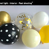 A collection of round balloons in gold, white, and black with gold confetti dots, photographed indoors.