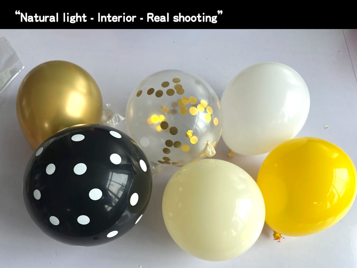 A collection of round balloons in gold, white, and black with gold confetti dots, photographed indoors.
