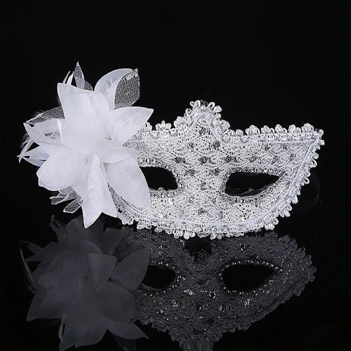 White feather rhinestone masquerade mask displayed on a reflective surface against a black background.