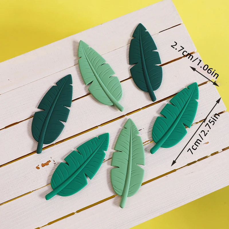 Un juego de cinco toppers de hojas de dinosaurio verde sobre una superficie de madera blanca.
