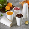 A collection of white disposable paper coffee cups filled with various beverages, including orange juice and red liquid.