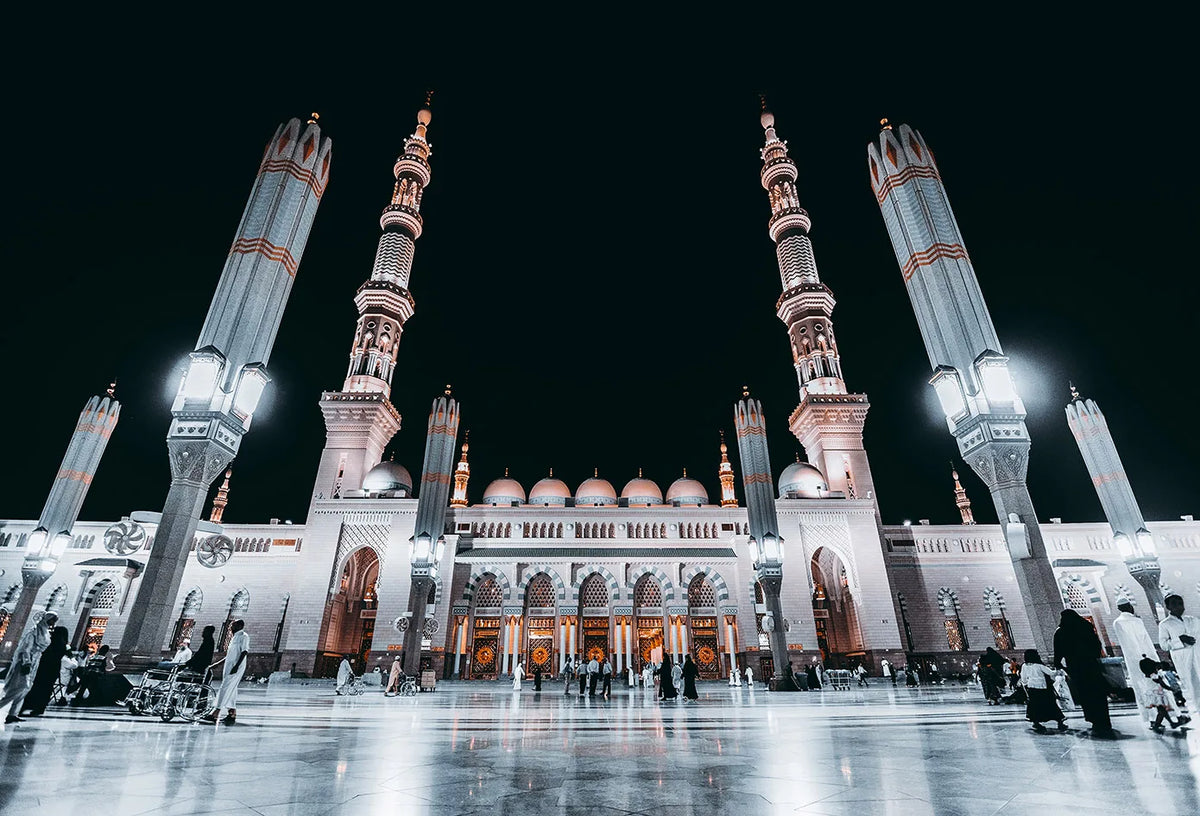 Night view of the Masjid an Nabawi with minarets and dome architecture.