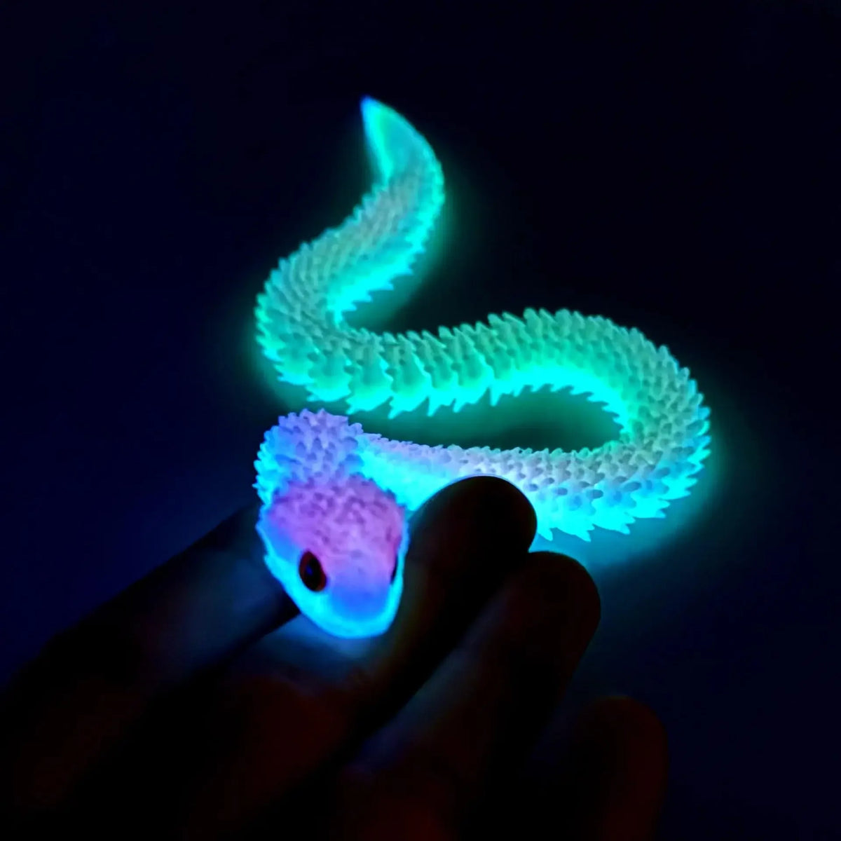 A hand holds a glowing, translucent green and purple 3D printed articulated snake fidget toy against a dark background.