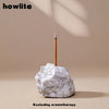 A clear quartz crystal is placed on a light-colored surface with a thin stick, suggesting an incense or aromatherapy product.