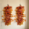 A pair of dried autumn sunflower and maple leaf swag decorations hanging on a white wall.