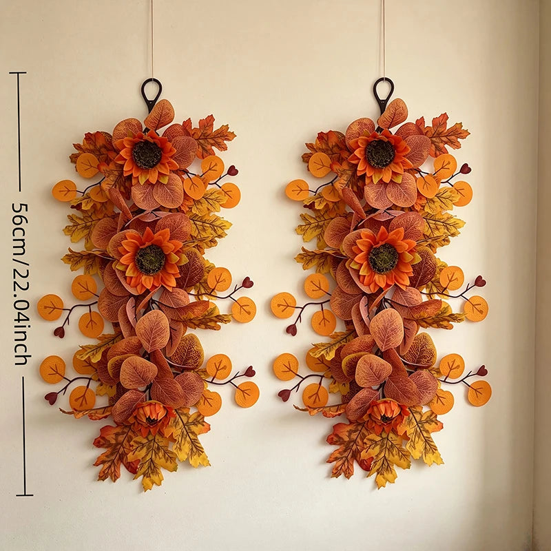A pair of dried autumn sunflower and maple leaf swag decorations hanging on a white wall.