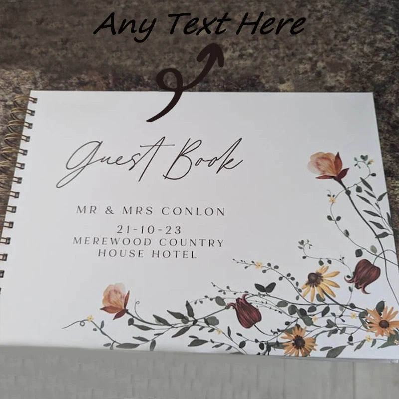 A white leather-bound guest book with elegant script text and floral watercolor design.