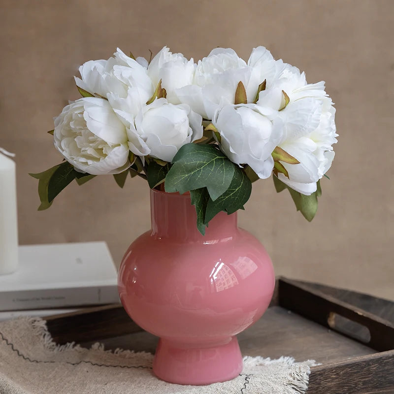 A bouquet of white artificial silk peonies in a pink vase on a wooden tray.