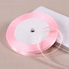 Pink satin ribbon spool with a thin ribbon unwinding on a white background.