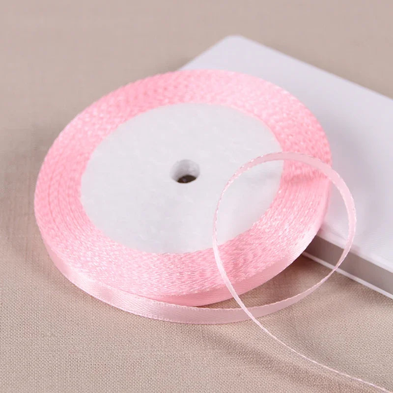 Pink satin ribbon spool with a thin ribbon unwinding on a white background.