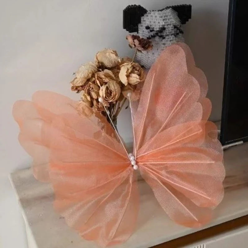 A peach colored silk artificial butterfly decoration with gold dried flowers and a small black and white cat figurine.