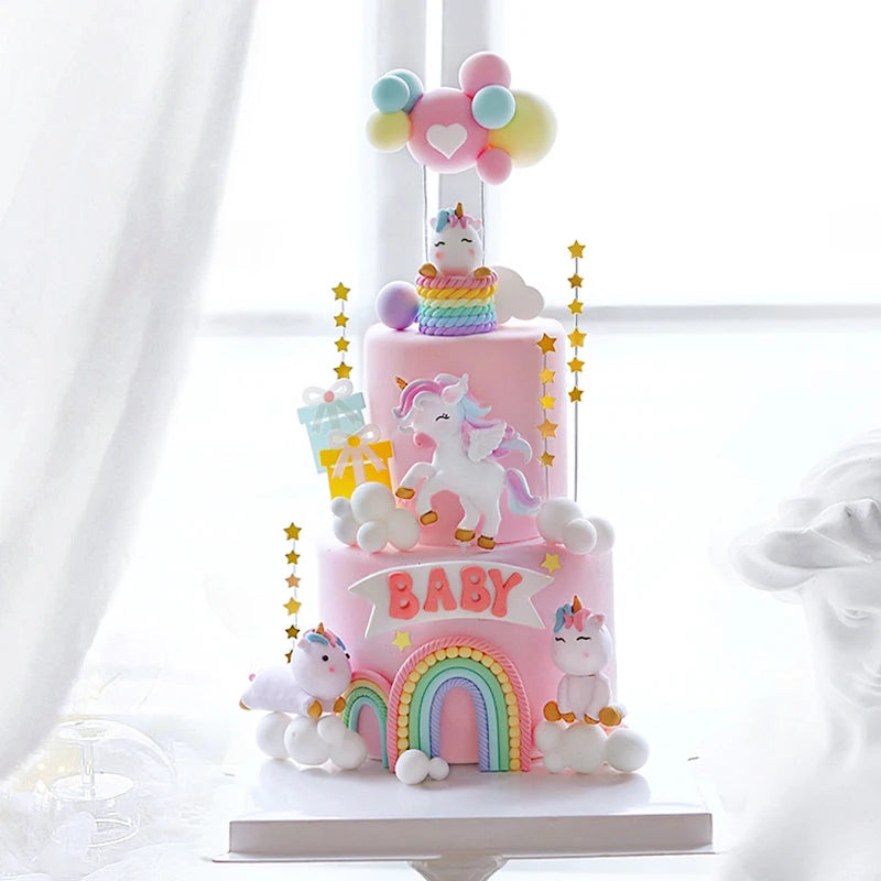 A pink unicorn theme cake topper set featuring a unicorn figure and colorful balloons on a tiered cake.