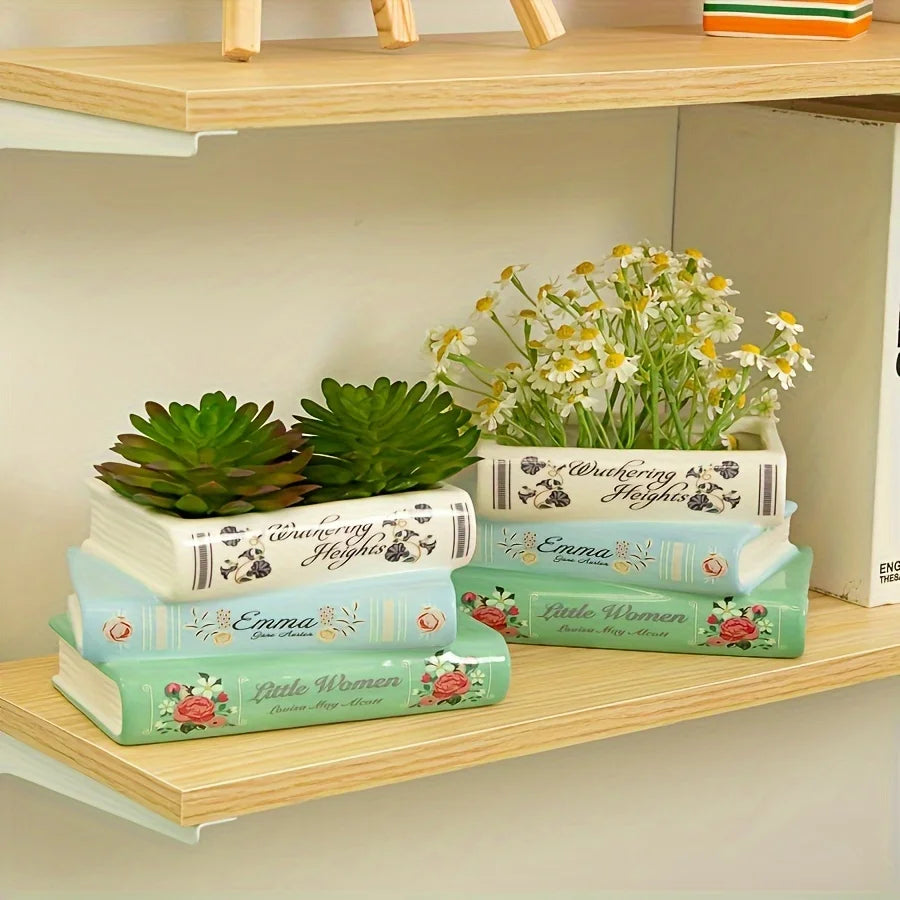 Présentation de trois vases en céramique en forme de livres aux tons verts et bleus, avec des fleurs séchées et de la verdure