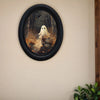 Oval wooden wall art depicting a ghost riding a bicycle in a forest scene.