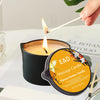 A lit massage candle in a black tin with a wooden stick, showing the E&D Massage Candle Flavour Amber Vanilla.