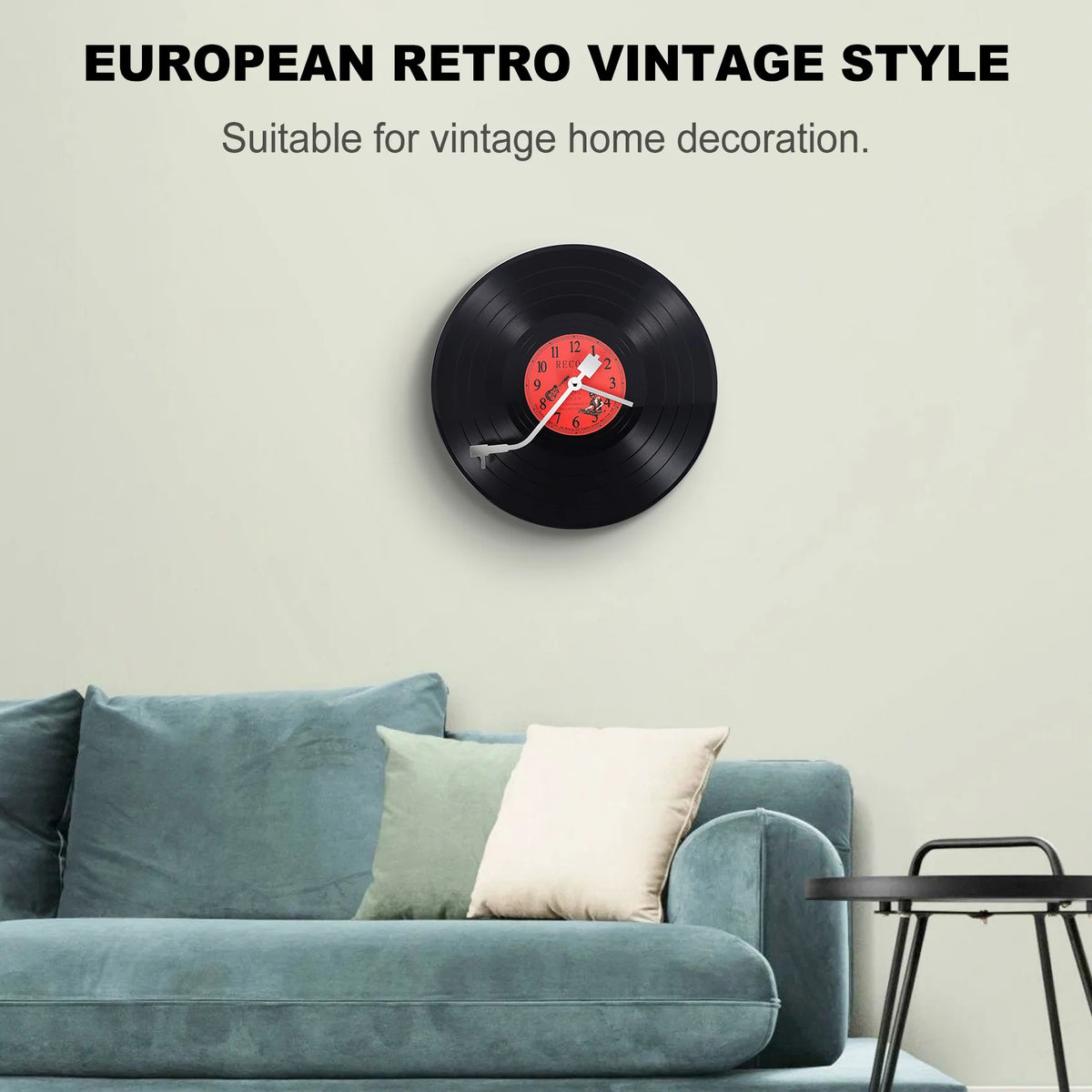 Schwarze Vinyl-Wanduhr mit rotem Zifferblatt auf heller Wand über einem türkisen Sofa.