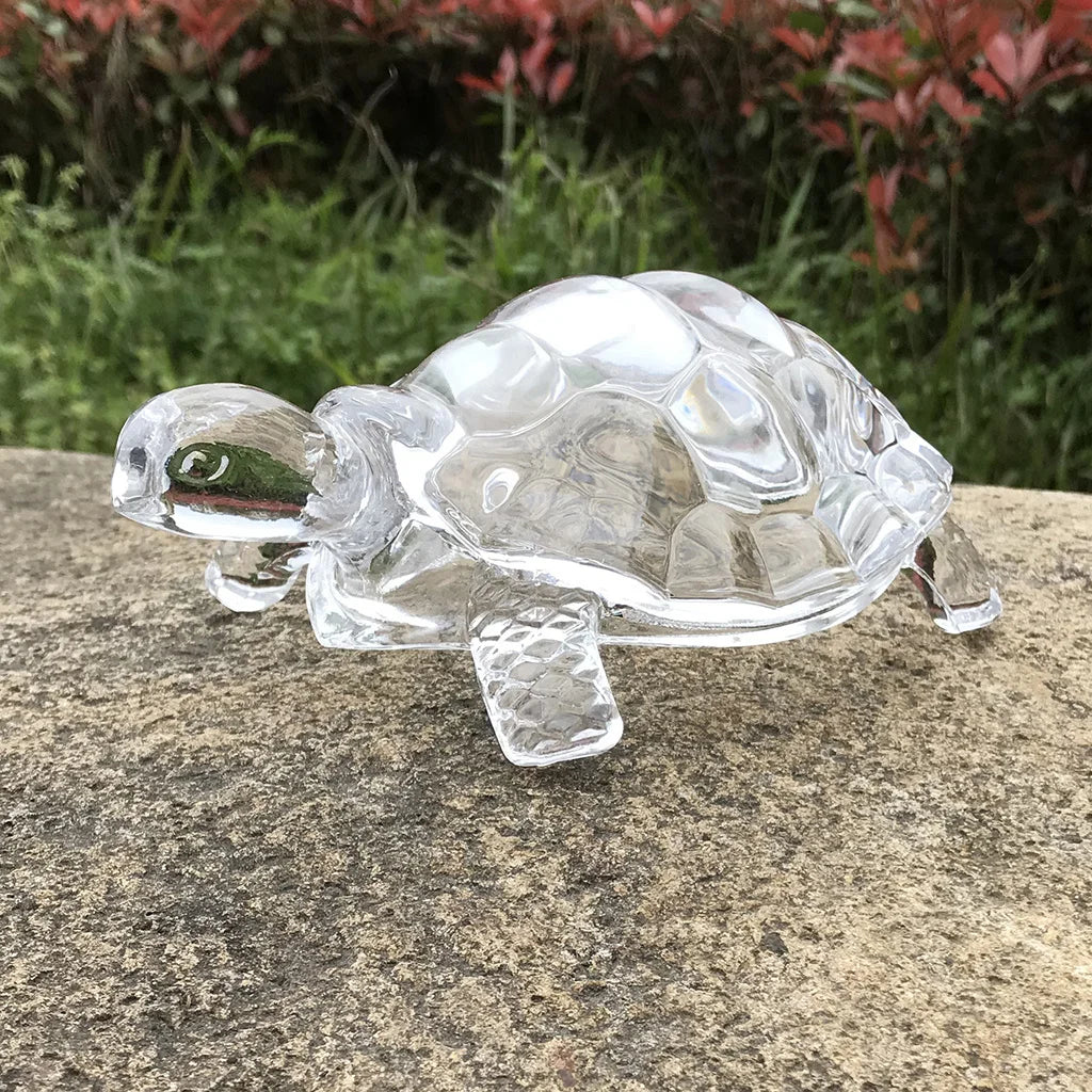 Clear glass miniature tortoise statue resting on a gray stone surface.