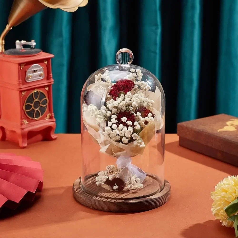 A glass dome cloche with a clear glass top and wooden base displaying dried flowers on an orange table.