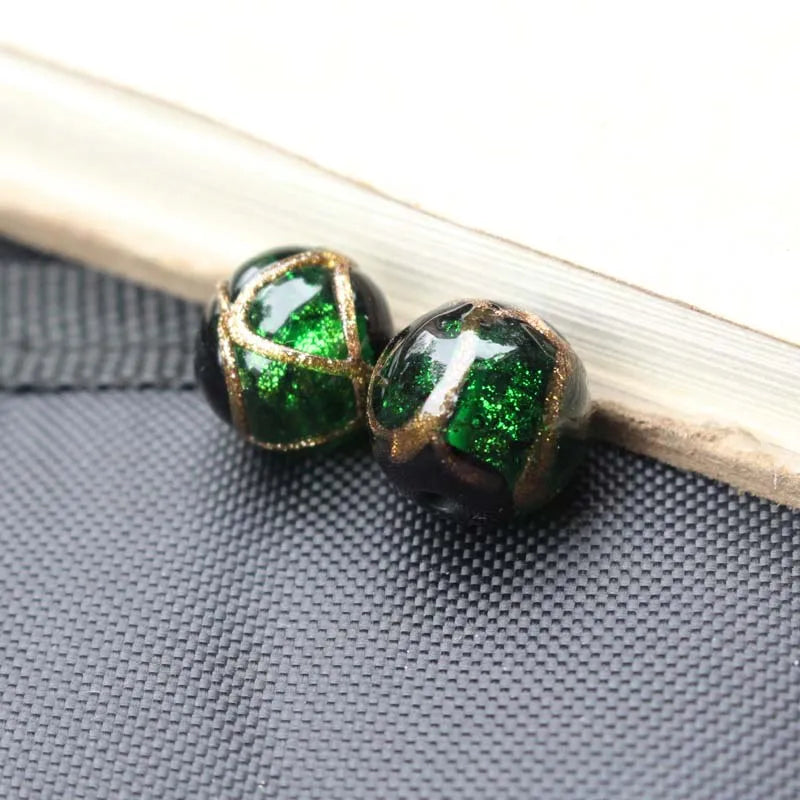 Two handcrafted lampwork glass beads with gold accents resting on a dark gray surface next to a wooden stick.