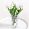 A bouquet of white artificial tulip flowers in a clear glass vase on a white plate.