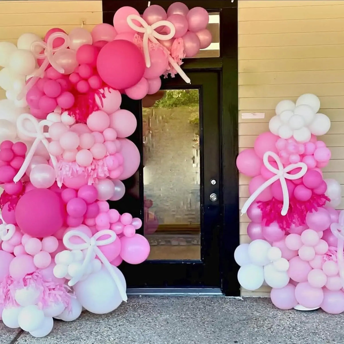 A large arrangement of pink and white balloons decorating a doorway for a party.