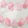Pink paper cherry blossom flower banner with white accents strung across a white background