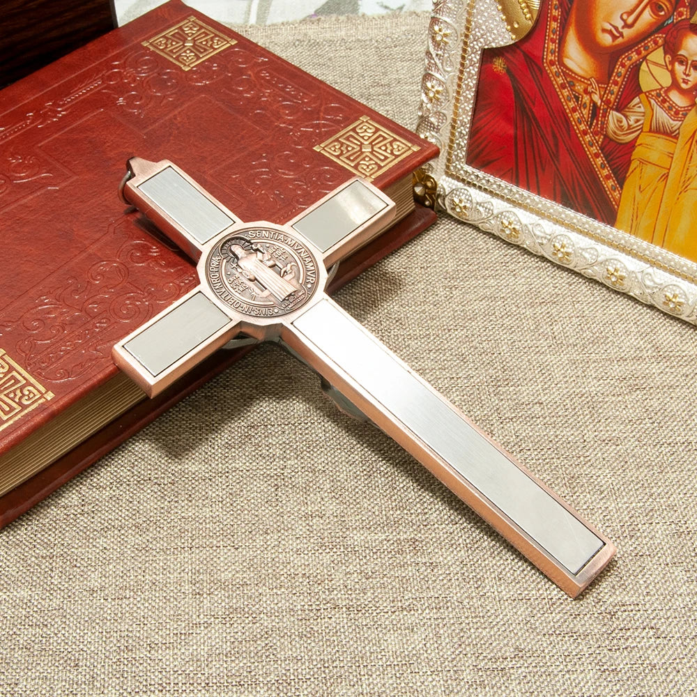 A silver crucifix wall decor featuring a St. Benedict medal and INRI inscribed on a red book, set against a beige background.