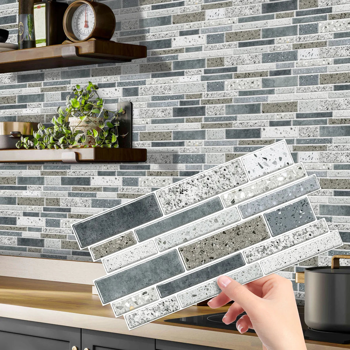 A hand is placing a rectangular crystal film marble wall decal onto a gray and white tiled backsplash.