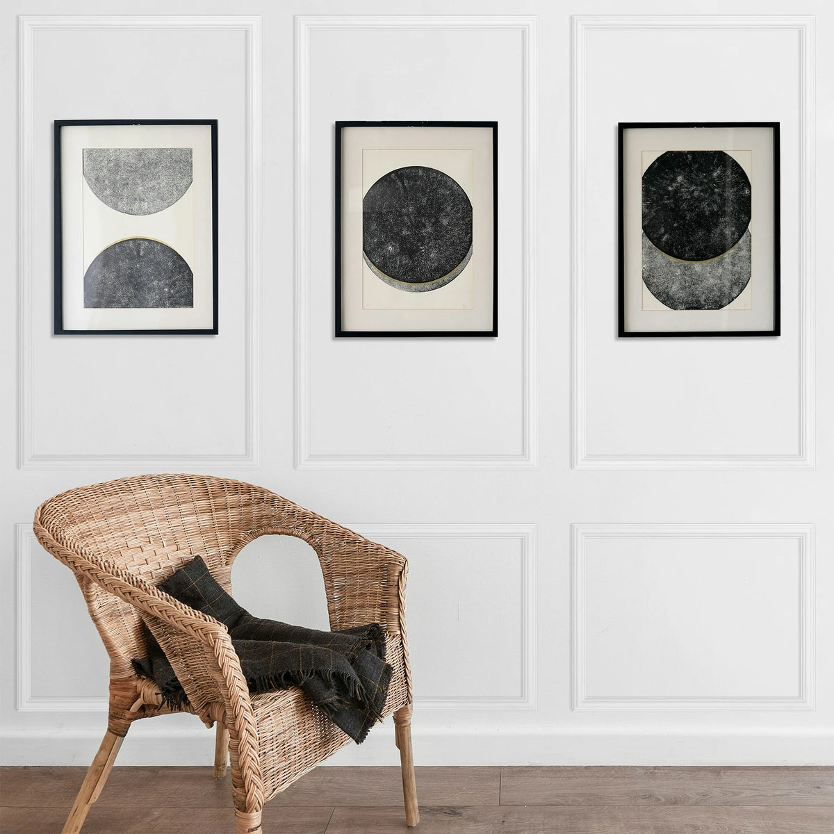 A woven wicker chair placed in front of a gallery wall featuring three framed abstract circular art pieces.