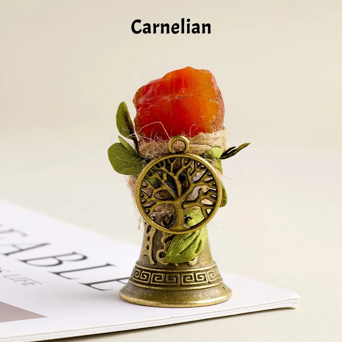 A natural crystal brass bell with a copper finish, decorated with green leaves and presented on a white surface.