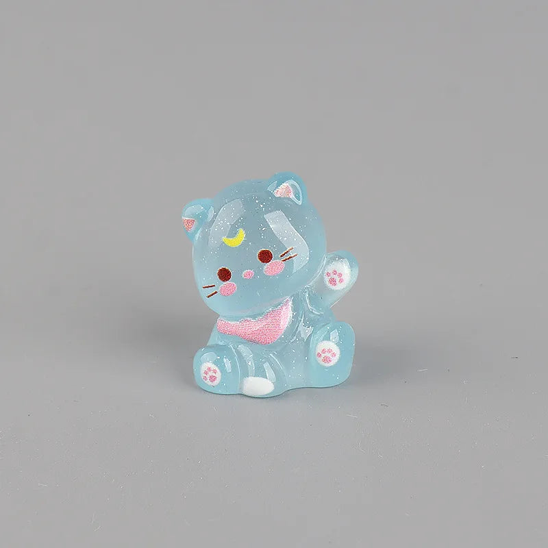 A small, translucent blue resin figurine of a cat with pink accents and a yellow crescent moon on its forehead.