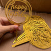 A hand holds a gold acrylic happy birthday cake topper, showing the intricate script design.