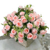 A bouquet of pink and peach artificial roses with green foliage arranged in a woven container.