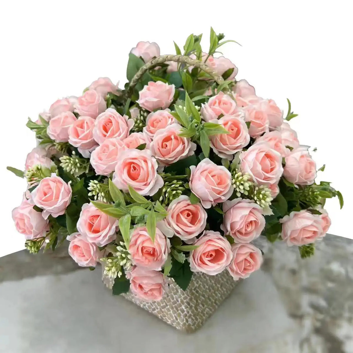 A bouquet of pink and peach artificial roses with green foliage arranged in a woven container.