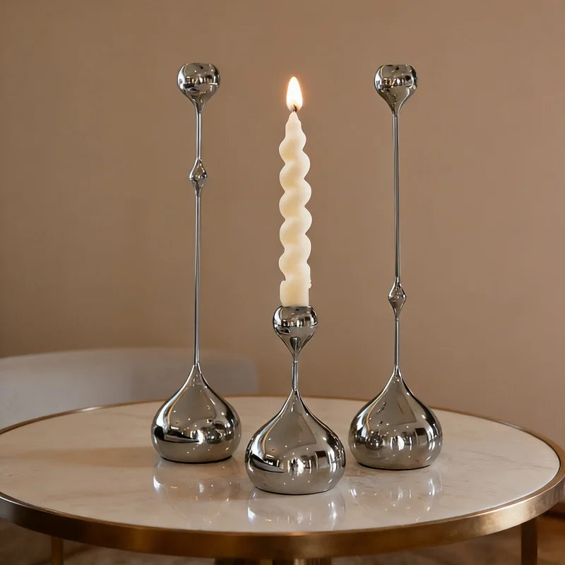 A set of three silver waterdrop design candle holders with lit candles displayed on a marble table.