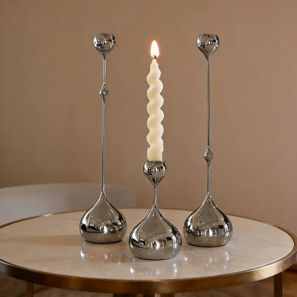 A set of three silver waterdrop design candle holders with lit candles displayed on a marble table.