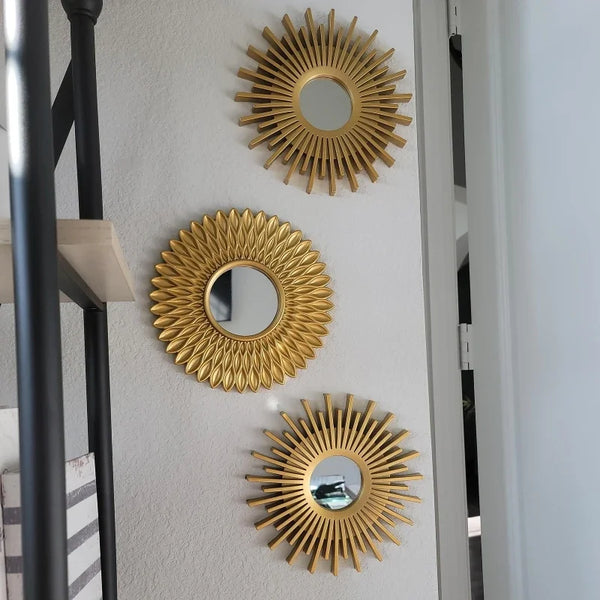 A set of three gold sunflower wall mirrors mounted on a white wall.