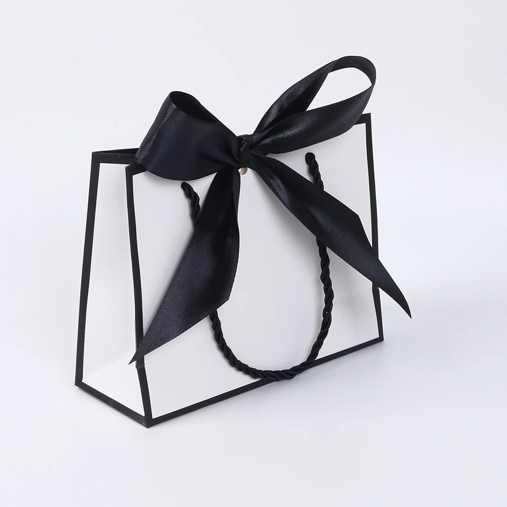 A set of five elegant black and white gift bags tied with black ribbon bows displayed in a square frame.