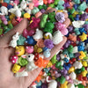 A hand holds a large collection of assorted resin miniature figurines in various colors and shapes for DIY decor.