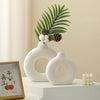 White ceramic vase with a donut pattern decorated with green palm leaves and pine cones.