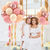 A woman in a white dress sits next to a young girl, surrounded by pink and gold balloons and confetti decor.