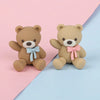 Two soft brown teddy bear figures with blue and pink bows displayed on a light pink and blue background.