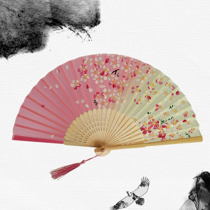A vintage bamboo folding hand fan with pink and cream floral patterns is shown against a white background.